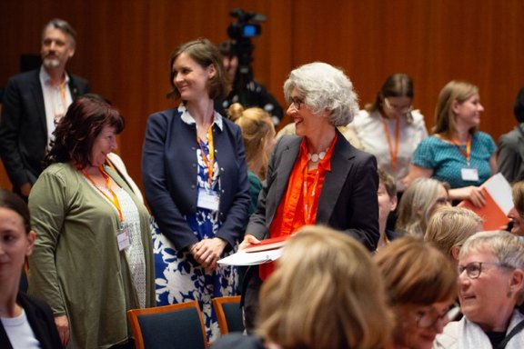 Telnehmer*innen im großen Saal angeregt im Gespräch mit einander, im Hintergrund die Kamera für die Live Aufzeichnung, bei der Abschlusskonferenz InnoGründerinnen 07.06.24